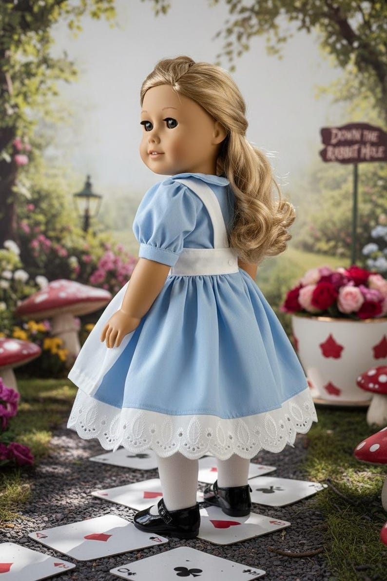 Peut inclure: Une poup&eacute;e aux cheveux blonds portant une robe bleu clair avec un tablier blanc, un ourlet en dentelle blanche, des collants blancs et des chaussures noires. La poup&eacute;e est plac&eacute;e dans un jardin avec un panneau indiquant Down the Rabbit Hole.