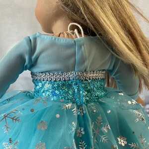 May include: A blue tulle dress with silver snowflake print and a sequined bodice. The dress has long sleeves and a fitted bodice.