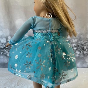 May include: A blue tulle dress with silver snowflake print and sequins. The dress has long sleeves and a fitted bodice.