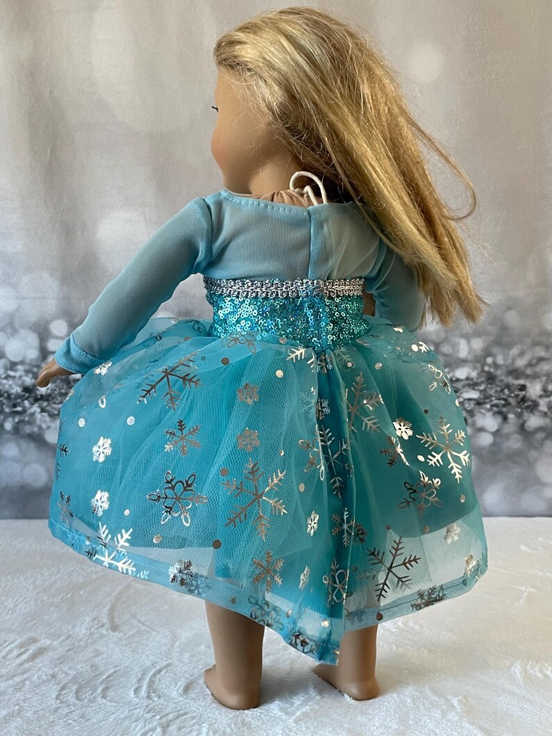 May include: A blue tulle dress with silver snowflake print and sequins. The dress has long sleeves and a fitted bodice.