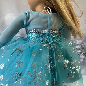 May include: A blue tulle dress with silver snowflake print and sequins. The dress has long sleeves and a fitted bodice.