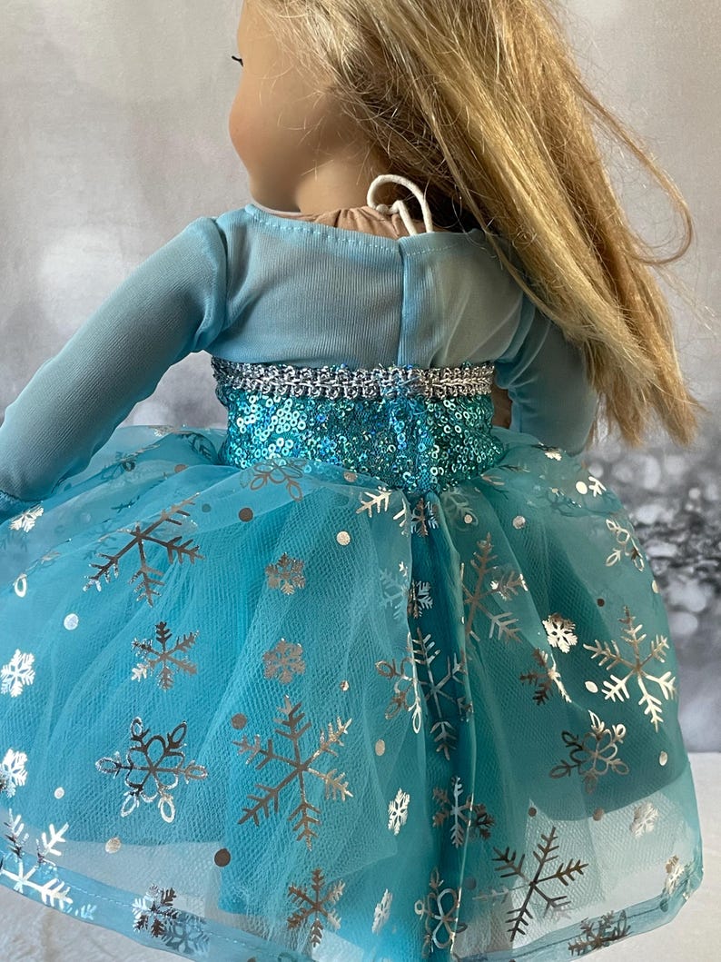 May include: A blue tulle dress with silver snowflake print and sequins. The dress has long sleeves and a fitted bodice.