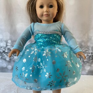 May include: A blue and silver dress with snowflake print for an 18-inch doll. The dress has a tulle skirt and a sequined bodice.