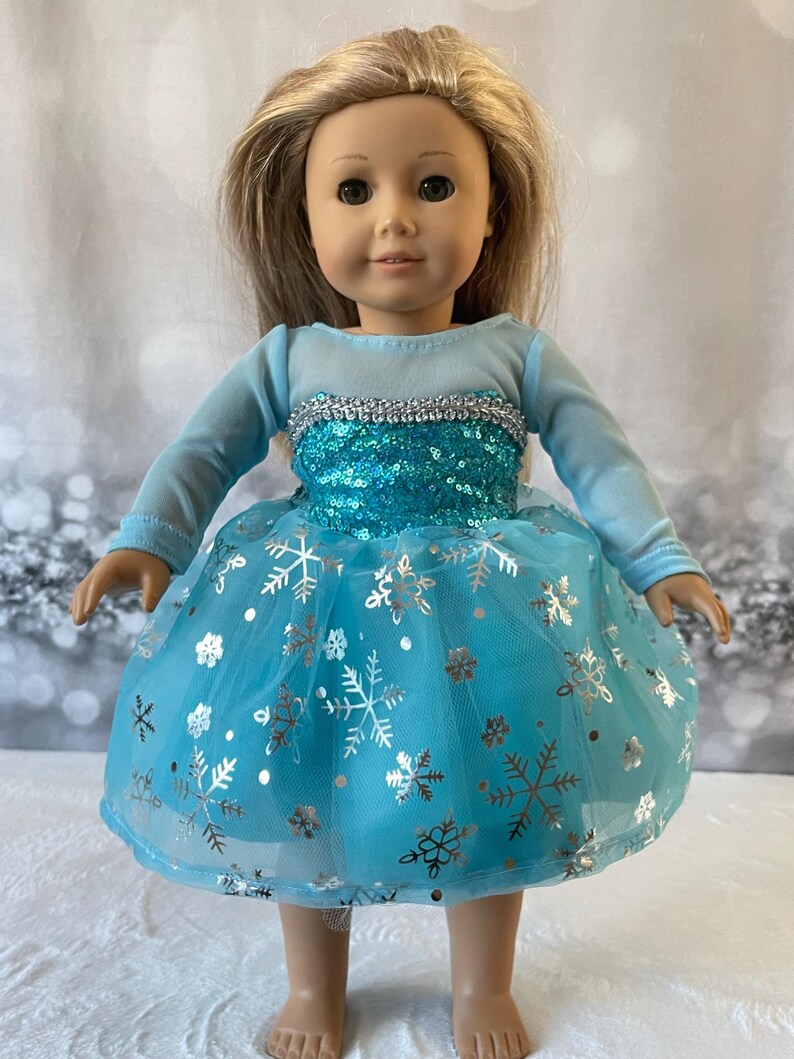 May include: A blue and silver dress with snowflake print for an 18-inch doll. The dress has a tulle skirt and a sequined bodice.