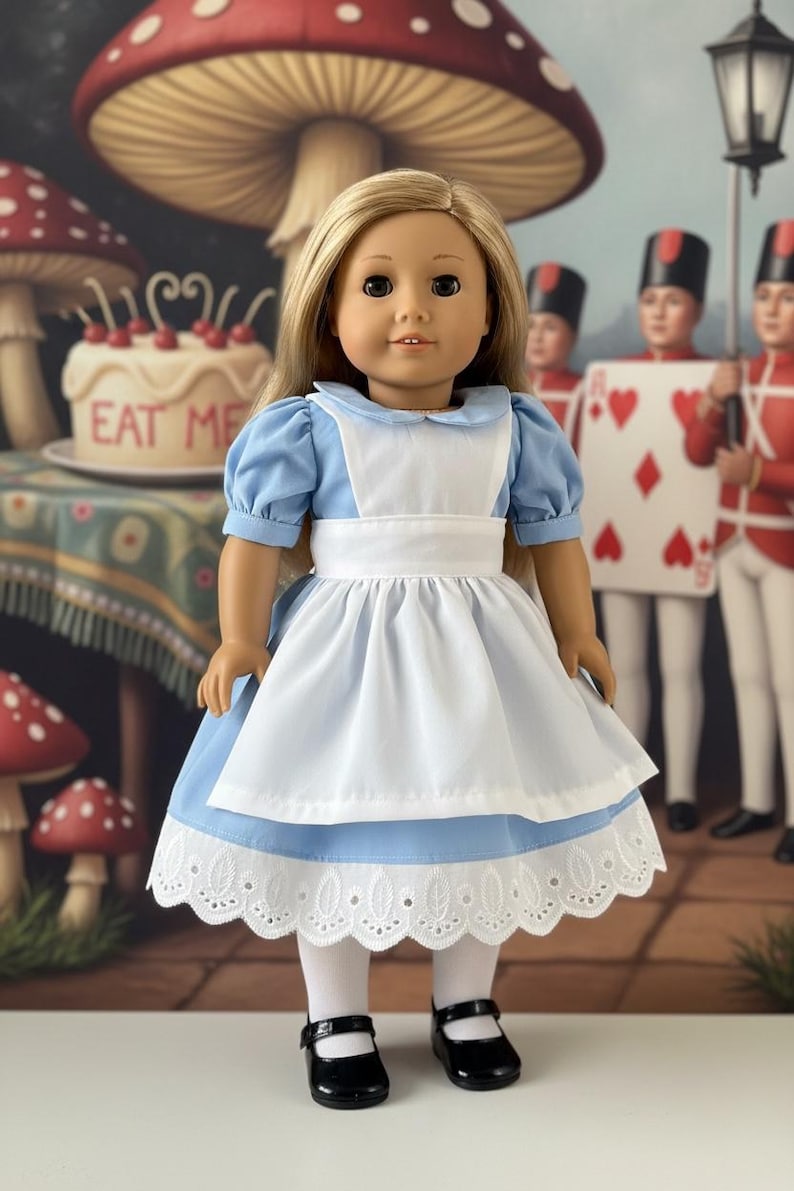 Peut inclure: Une poup&eacute;e aux longs cheveux blonds portant une robe bleu clair &agrave; manches courtes bouffantes, un tablier blanc et une bordure en dentelle blanche &agrave; l'ourlet. La poup&eacute;e porte &eacute;galement des collants blancs et des chaussures noires &agrave; bride.