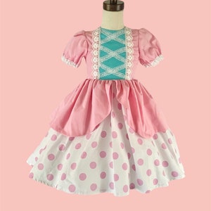 May include: A pink and white polka dot dress with a turquoise bodice and white lace trim. The dress has a puffy skirt and short sleeves.