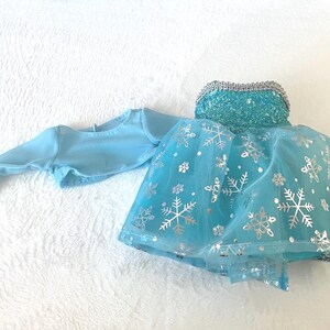 May include: A light blue tulle dress with silver snowflake accents and a matching light blue long-sleeved top. The dress has a sequined bodice.