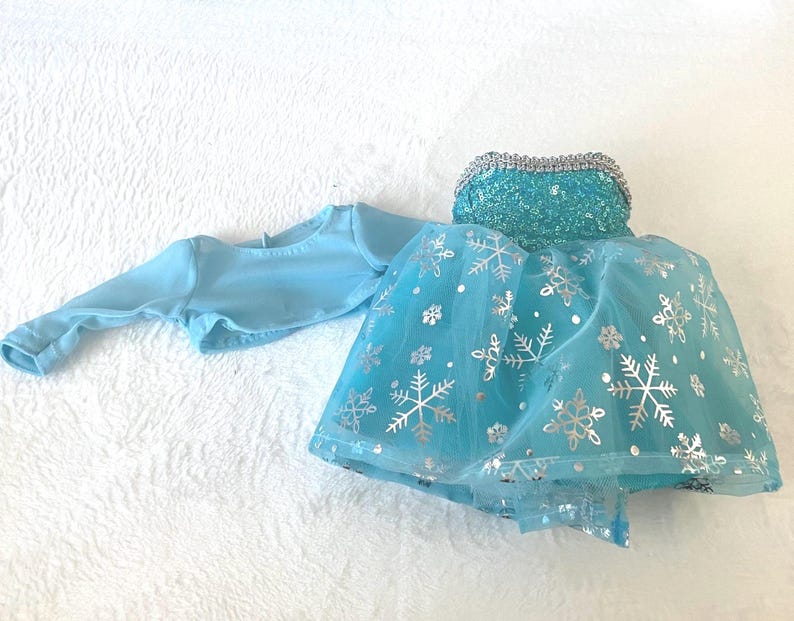 May include: A light blue tulle dress with silver snowflake accents and a matching light blue long-sleeved top. The dress has a sequined bodice.