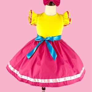May include: A yellow and pink dress with a blue ribbon and a pink bow headband. The dress has a ruffled neckline and sleeves.