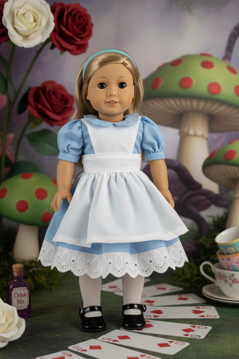 Peut inclure: Une poup&eacute;e aux cheveux blonds avec un bandeau bleu clair, v&ecirc;tue d'une robe bleu clair &agrave; col blanc, d'un tablier blanc et de collants blancs. La poup&eacute;e porte des chaussures noires &agrave; brides et se tient debout avec une expression neutre.