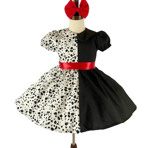 May include: A black and white dalmatian print dress with a black half and a red ribbon. The dress has a white collar and short sleeves.