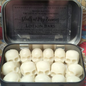 May include: A black metal tin filled with white lotion bars shaped like skulls. The tin's lid has text that reads "Skulls of My Enemies Lotion Bars" and the Etsy shop's URL. The lotion bars are arranged neatly inside the tin.
