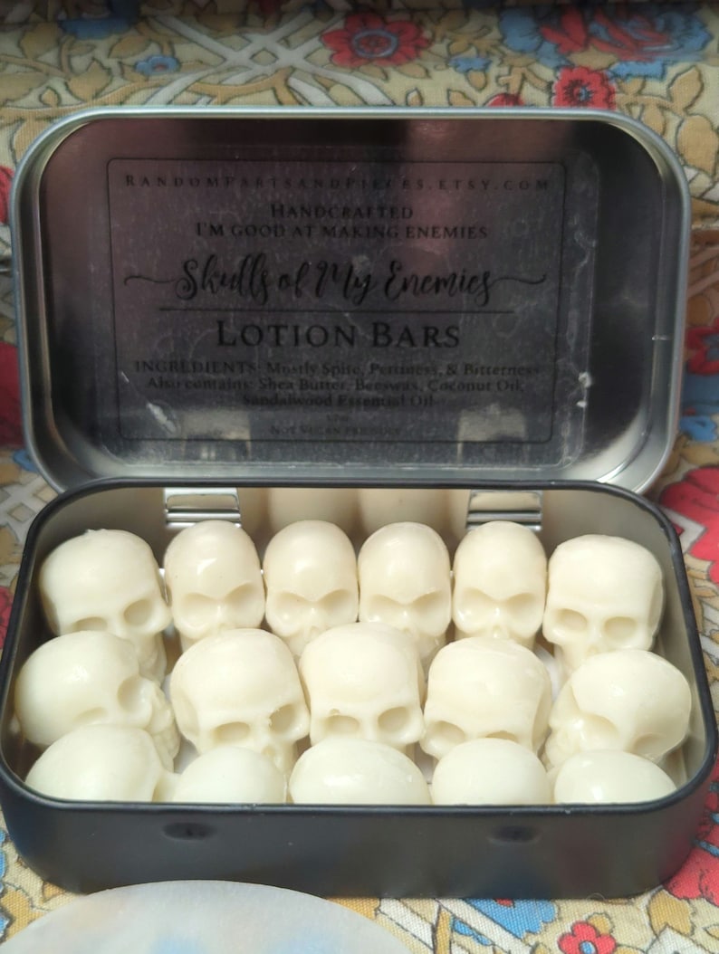 May include: A black metal tin filled with white lotion bars shaped like skulls. The tin's lid has text that reads "Skulls of My Enemies Lotion Bars" and the Etsy shop's URL. The lotion bars are arranged neatly inside the tin.