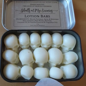 May include: An open metal tin filled with white skull-shaped lotion bars. The tin's label reads "Skulls of My Enemies" and lists ingredients like shea butter and coconut oil. The bars are arranged neatly inside the tin.