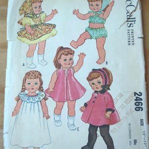 May include: A vintage McCall's sewing pattern for a doll's wardrobe. The pattern is for a 12-13 inch doll and includes a dress, swimsuit, nightgown, and coat. The pattern is printed on white paper with a pink, green, and blue colour scheme. The pattern number is 2466 and the price is 50 pence.