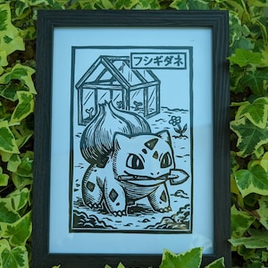 May include: Black and white framed print featuring a Bulbasaur illustration with a greenhouse and Japanese text. The artwork is set against a backdrop of green and yellow ivy.