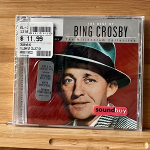 Peut inclure: Un boîtier de CD avec un fond rouge représentant une photo de Bing Crosby portant un fedora vert. Le texte "The Best of Bing Crosby" et "The Millennium Collection" est imprimé en blanc sur le boîtier. Le boîtier de CD est étiqueté "Soundbuy" en rouge.