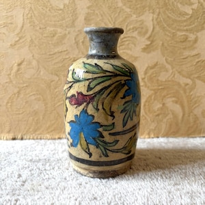 Może przedstawiać: Mały, ceramiczny wazon z wąską szyjką i pękatym korpusem. Wazon jest pomalowany w niebieskie, zielone i czerwone wzory kwiatowe na kremowym tle. Obręcz jest szara, a podstawa ma ciemny pas.