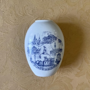 Può includere: Vaso bianco in ceramica a forma di uovo con un'illustrazione blu dei monumenti di Copenaghen. Il design include la statua della Sirenetta e la parola "KOBENHAVN" in basso. Il vaso ha una finitura liscia e lucida.