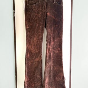May include: A pair of dark brown corduroy pants featuring a bleached, mottled pattern throughout. These pants have a classic five-pocket design, a button and zipper fly closure, and a straight-leg cut that flares slightly toward the bottom hem.