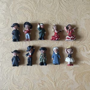 May include: A collection of ten small figurines, each depicting a different character. The figurines are made of painted plastic and feature a variety of colors, including red, blue, green, black, and white. The figurines are all standing upright and are arranged in a row.