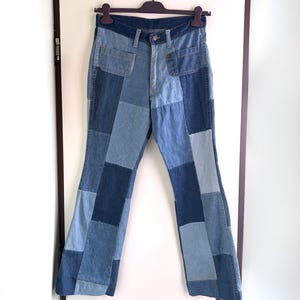 Op de afbeelding: Denim broek met hoge taille en een patchwork ontwerp in diverse blauwtinten, waaronder licht-, midden- en donkerblauwe panelen. De broek is voorzien van een knoop- en ritssluiting, twee voorzakken en een uitlopende broekspijp.