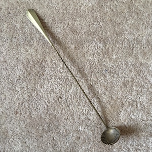 Può includere: Un cucchiaio da bar argentato con manico attorcigliato e coppetta a forma di conchiglia. Il cucchiaio ha un'estremità piatta a forma di goccia per mescolare. Il cucchiaio è lungo circa 30 cm.