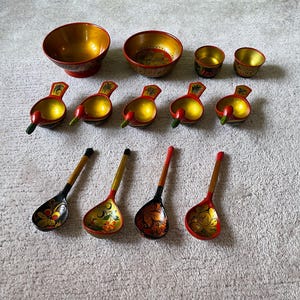 Puede incluir: Un conjunto de 12 cuencos y cucharas de madera pintados a mano en rojo, dorado y negro con diseños florales y de pájaros. Los cuencos son de varios tamaños y formas, y las cucharas son todas del mismo tamaño.