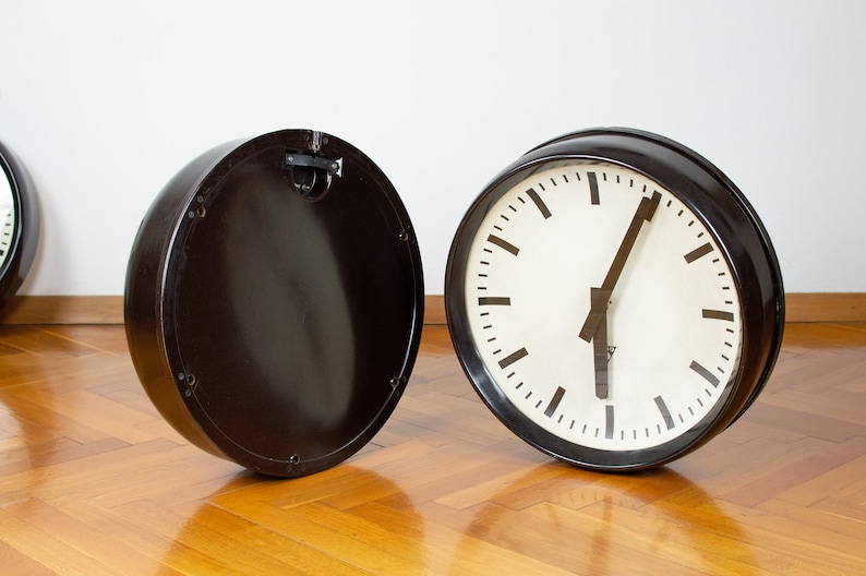 K&ouml;nnte beinhalten: Eine schwarze Vintage-Uhr mit wei&szlig;em Zifferblatt und schwarzen Zeigern. Die Uhr ist von ihrem R&uuml;cken getrennt, wodurch das Innenleben sichtbar wird.