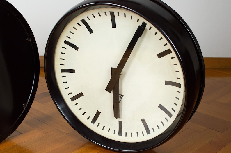 K&ouml;nnte beinhalten: Eine schwarze Uhr mit wei&szlig;em Zifferblatt und schwarzen Zeigern. Die Uhr hat eine schwarze L&uuml;nette und einen wei&szlig;en Hintergrund. Die Uhr befindet sich auf einer Holzoberfl&auml;che.