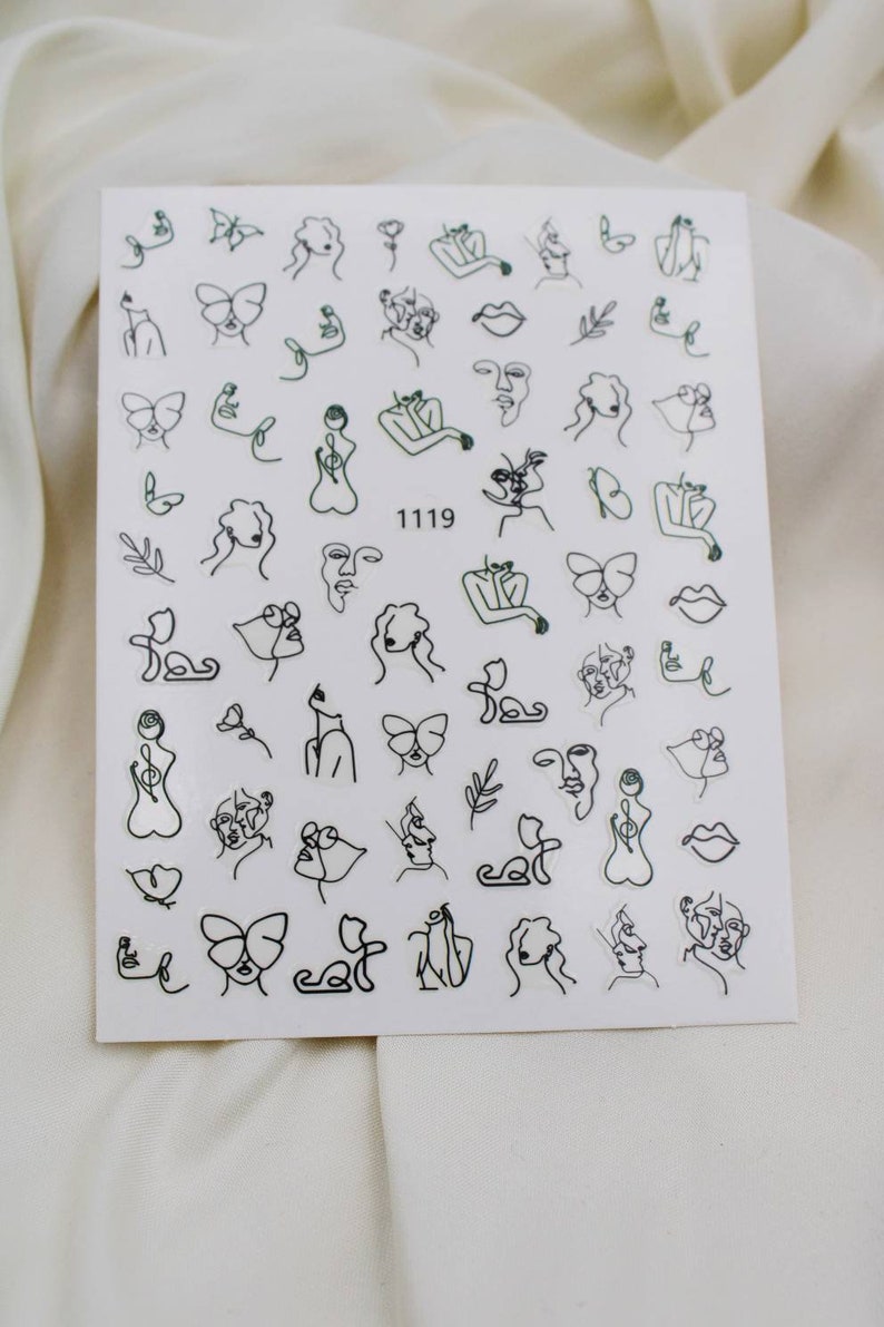 May include: A sheet of white nail stickers with black line drawings of faces, butterflies, flowers, and other abstract designs. The sheet has the number 1119 printed on it.