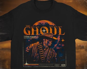 Puede incluir: Camiseta negra de cuello redondo con un gráfico retro. El diseño presenta el texto "THE GHOUL" sobre una ilustración de una figura con sombrero y chaqueta, sobre un planeta. El gráfico es en naranja, azul y blanco.