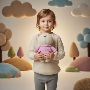 Peut inclure: Un enfant tenant un ours en peluche fait à la main. L'ours est principalement blanc cassé avec un pull rose. L'arrière-plan présente des éléments de paysage tricotés doux, notamment des arbres et des nuages, dans des tons beiges, roses et bleus.