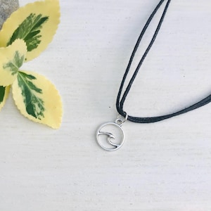 Peut inclure: Un collier en cordon noir avec un pendentif en forme de vague argenté. Le pendentif est un cercle avec un motif de vague à l'intérieur.