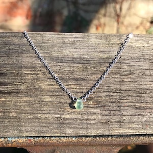 May include: A silver chain necklace with a single light green teardrop-shaped pendant.