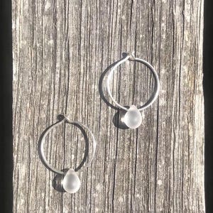 May include: A pair of silver hoop earrings with a clear teardrop-shaped charm hanging from each hoop.
