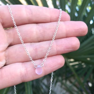 May include: A delicate silver chain necklace with a single, small, light pink glass bead pendant.