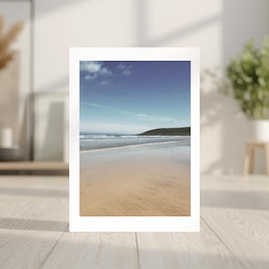 Könnte beinhalten: Ein gerahmter Druck mit einer Strandlandschaft mit Sand, Wellen und blauem Himmel. Der Druck wird auf einem hellen Holzboden präsentiert. Das Bild erzeugt ein Gefühl der Ruhe.
