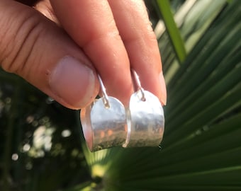 May include: A pair of silver hoop earrings with a hammered texture. The earrings are slightly curved and have a simple design.
