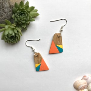 May include: A pair of geometric wooden earrings with a teal, orange and yellow colour scheme. The earrings are painted with a geometric pattern and have silver hooks.