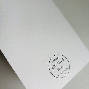 K&ouml;nnte beinhalten: Eine wei&szlig;e Karte mit einem schwarzen runden Stempel, auf dem "Handmade Little Thumb Design with lots of love" in handschriftlicher Schrift steht.