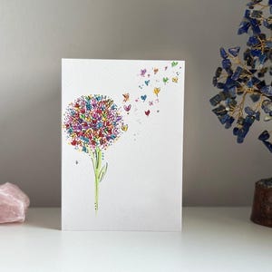 K&ouml;nnte beinhalten: Eine wei&szlig;e Karte mit einer bunten Illustration einer Blume mit Herzen als Bl&uuml;tenbl&auml;tter. Die Herzen fliegen auch von der Blume weg.