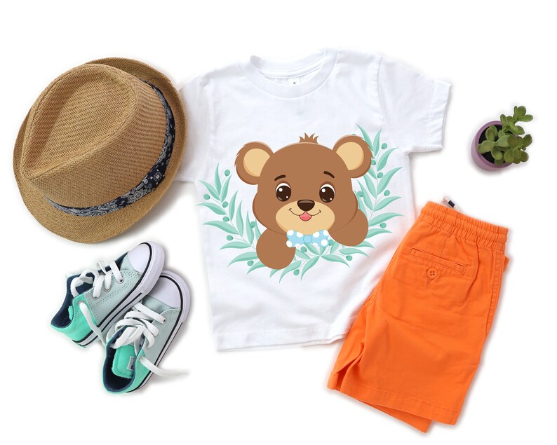 K&ouml;nnte beinhalten: Ein wei&szlig;es T-Shirt mit einem braunen B&auml;ren, der eine blaue Schleife tr&auml;gt, in einem gr&uuml;nen Bl&auml;tterrahmen. Der B&auml;r schaut den Betrachter an. Das Shirt wird mit orangefarbenen Shorts und gr&uuml;n-blauen Turnschuhen kombiniert.
