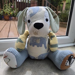 May include: A stuffed animal toy shaped like a dog, constructed from various fabric patches. The body features blue elephant patterns, while the limbs are made of textured light blue and yellow fabric. It has black button eyes and a black nose.