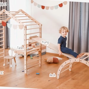 May include: Wooden play structure with a climbing wall, ramp, arch, and table. The structure is made of natural wood and has a light brown finish. A child is sitting on the ramp, which is attached to the climbing wall. The arch is on the right side of the image, and the table is on the left side. The structure is labeled with the words "Small Triangle", "Large Triangle", "Ramp", "Arch", and "Table".