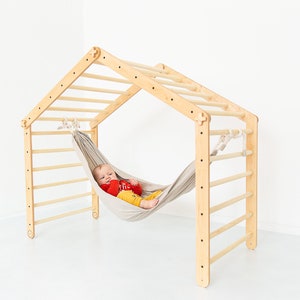 May include: A wooden climbing frame with a hammock attached. A baby is lying in the hammock.