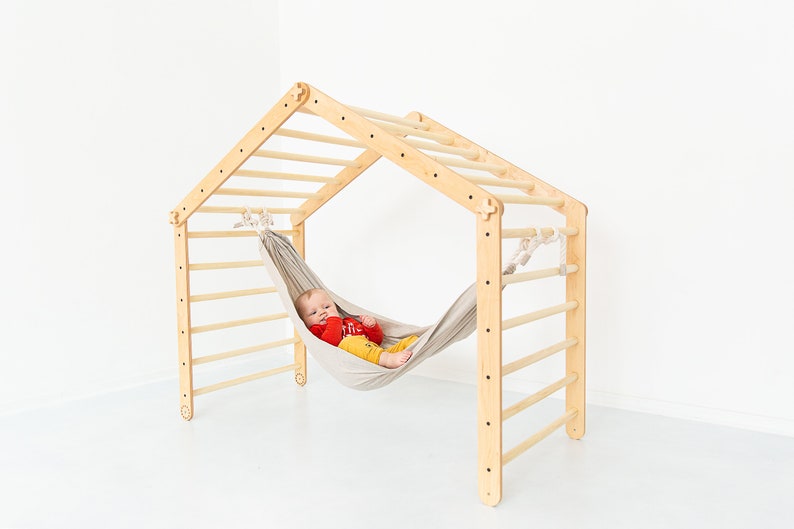 May include: A wooden climbing frame with a hammock attached. A baby is lying in the hammock.