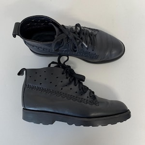 May include: A pair of black leather ankle boots with lace-up closures. The boots have a rounded toe, a low heel, and decorative stitching along the seams. The upper part of the boot features small, evenly spaced perforations.