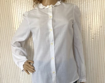 May include: A white long-sleeved button-up shirt with a frilled collar and cuffs. The shirt is made of a lightweight fabric and has a relaxed fit.
