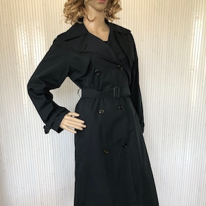 May include: A black double-breasted trench coat with a belt. The coat has a classic design and is made of a smooth fabric.